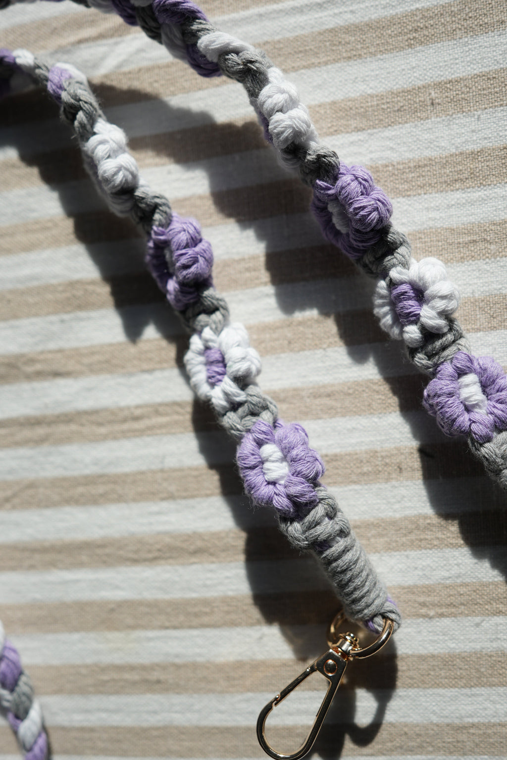 Floral keychain strap with purple and white flowers on a striped fabric background