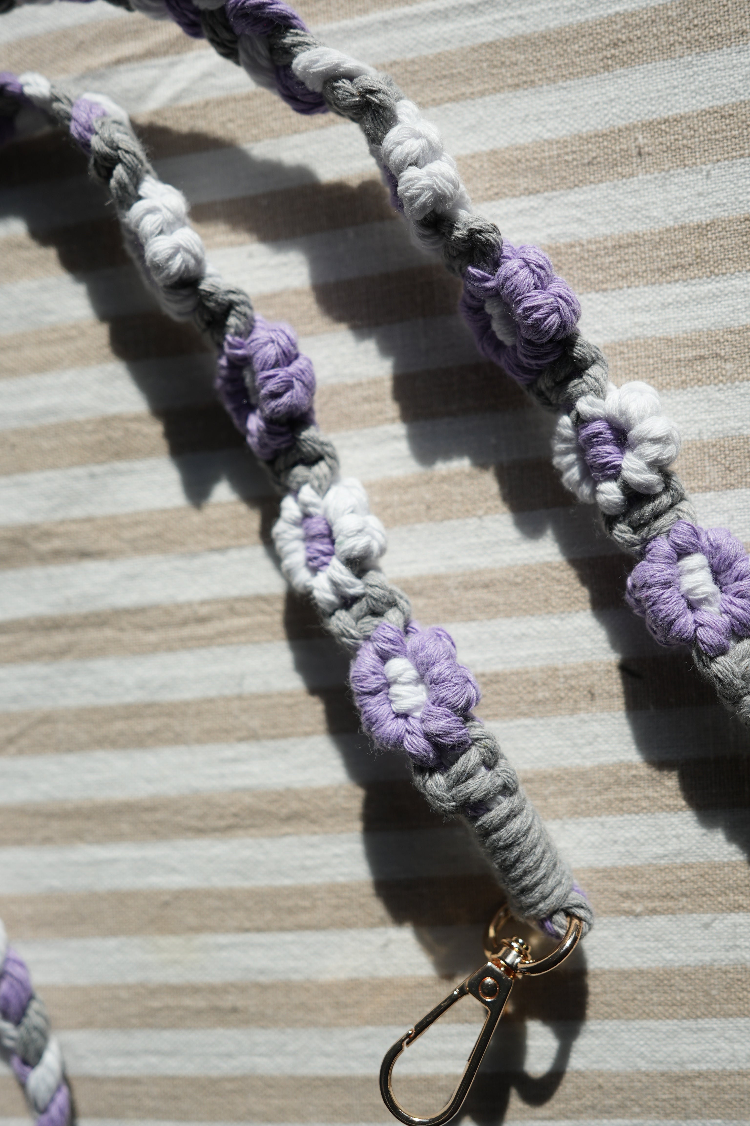 Floral keychain strap with purple and white flowers on a striped fabric background